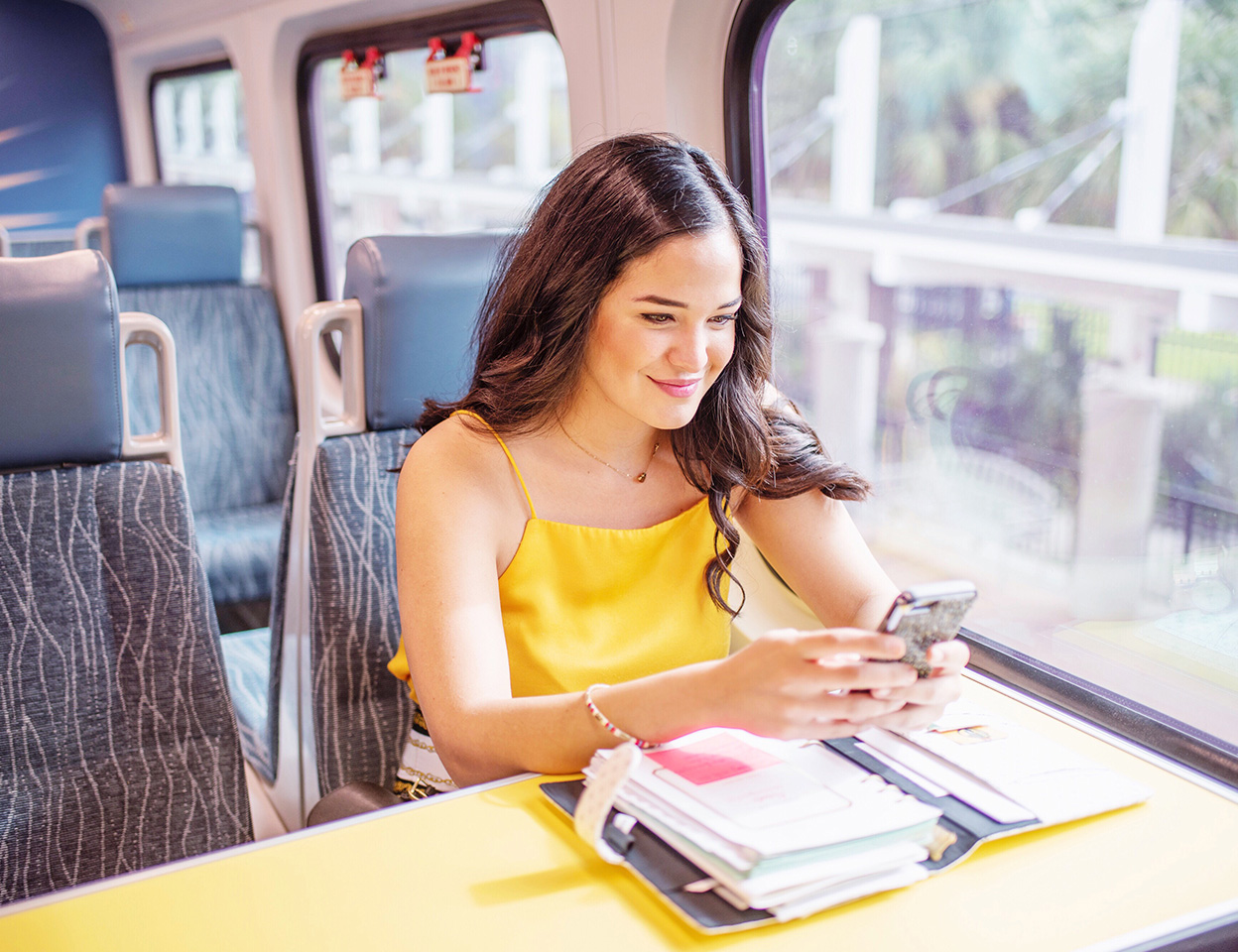 Young woman riding SunRail looking at phone and working in day planner.