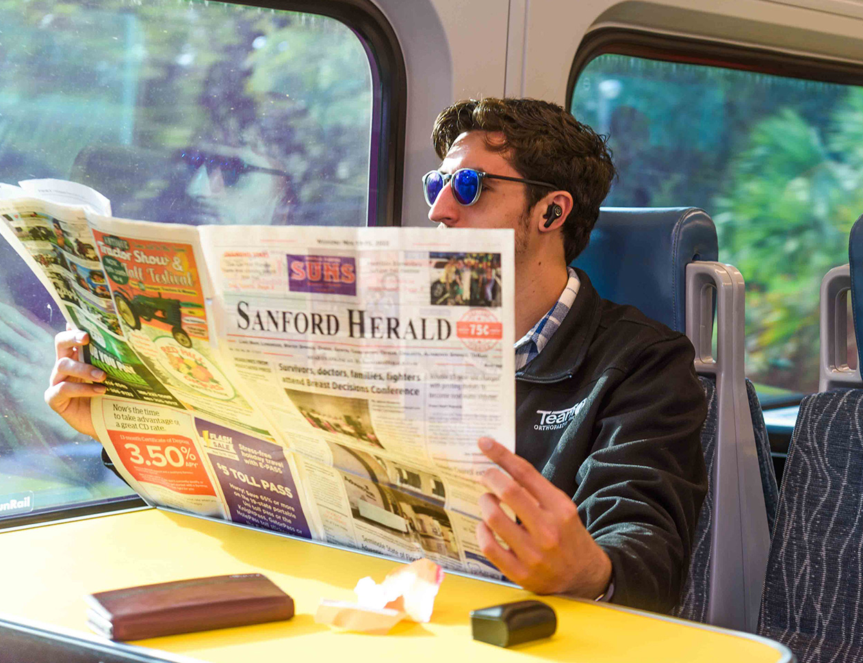 Man riding SunRail reading a Sanford Herald newspaper.