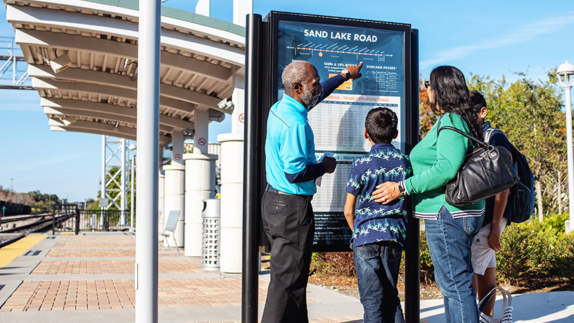 Landing Page image - SunRail Ambassador helping family at a schedule kiosk
