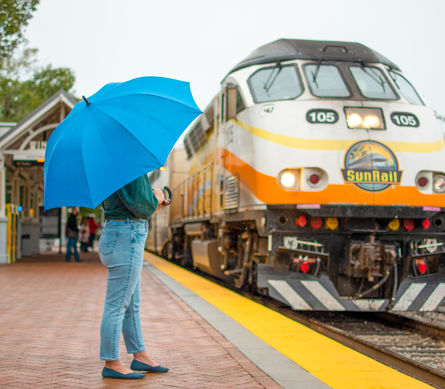 Woman with umbrella at Winter Park Station watching SunRail Train Arrive.