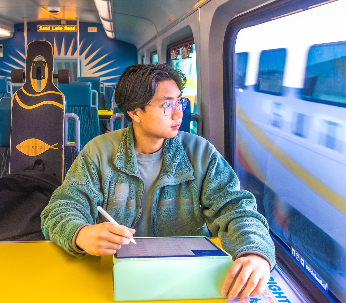 Young Student riding SunRail while working on tablet.