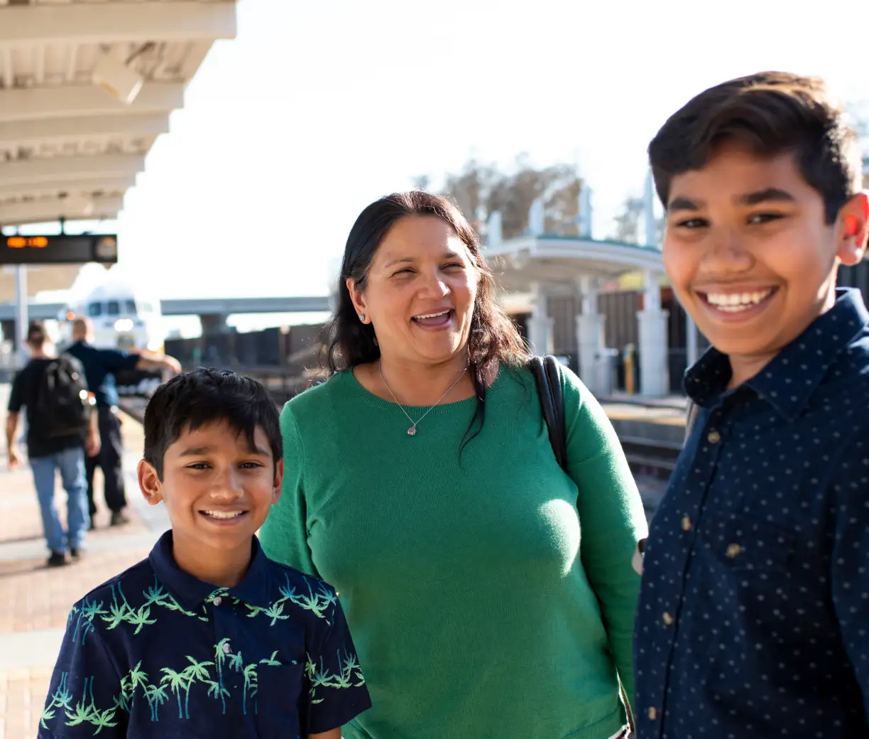 A mother and two boys wait at a SunRail station while the train approaches in the backgroudn.