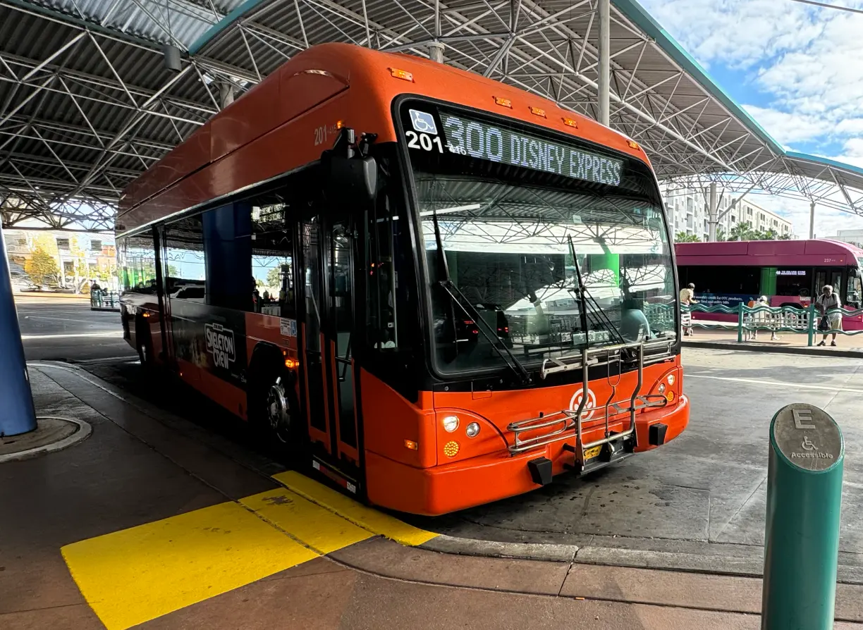 Two men exiting the Sanford Trolley. LYNX bus awaits for passengers in front of the ADA pedestrian route at LYNX Central.