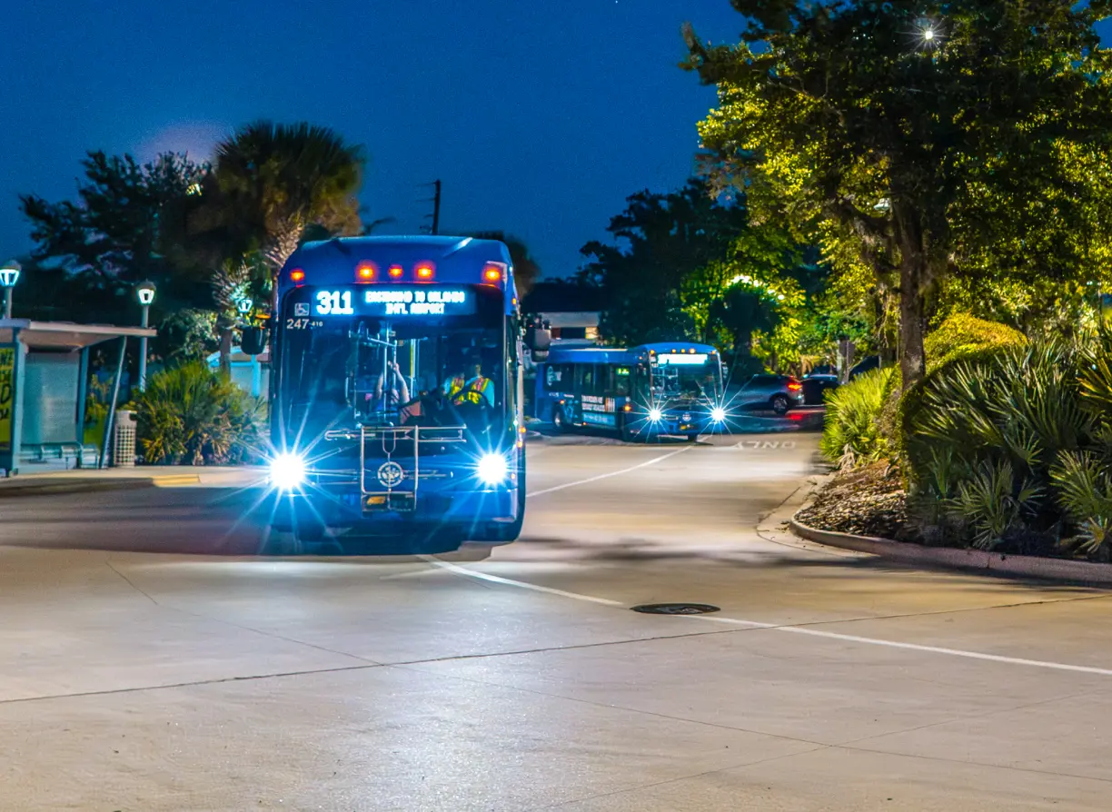 Two men exiting the Sanford Trolley. LYNX buses enter the parking lot at a SunRail station.