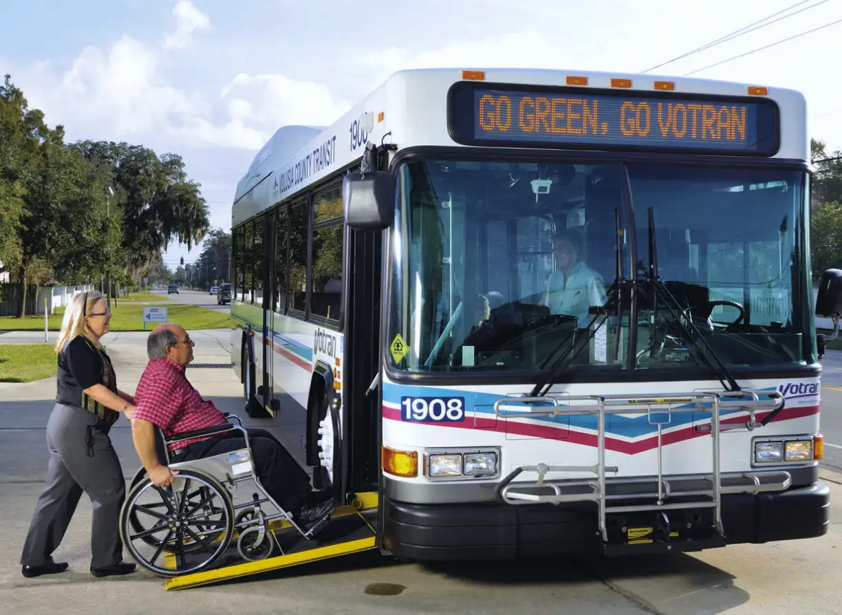 Woman assisting man in wheelchair onto Votran bus.
